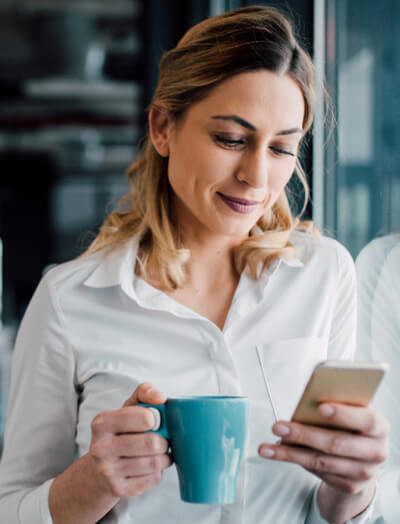 Smartly dressed office worker with a coffee mug and smartphone in her hands 
